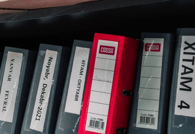 Color-coded office binders organized neatly in a storage shelf, featuring labels and a striking red binder.